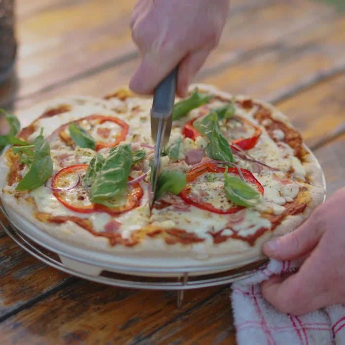 Person cutting a pizza with a fork and knife on a wooden table