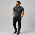 A man modeling a dark gray short-sleeve polo shirt and black jogger pants against a solid gray studio background.