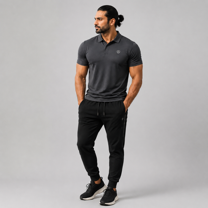 A man modeling a dark gray short-sleeve polo shirt and black jogger pants against a solid gray studio background.