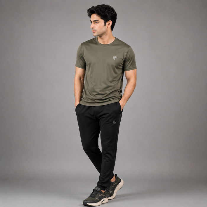 A man wearing an olive green short-sleeve athletic t-shirt and black athletic pants, standing against a solid gray studio background.