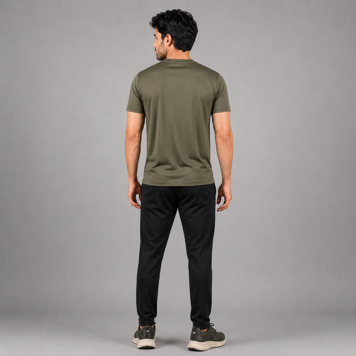A man viewed from behind wearing an olive green short-sleeve t-shirt and black pants, standing against a solid gray studio background.