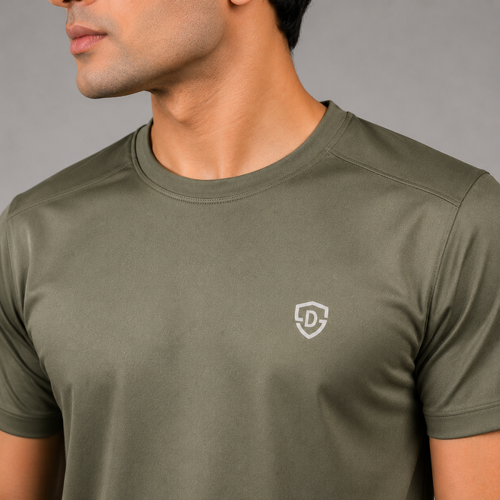A close-up of a man wearing an olive green athletic t-shirt with a small Dominance logo on the left chest, set against a neutral gray background.