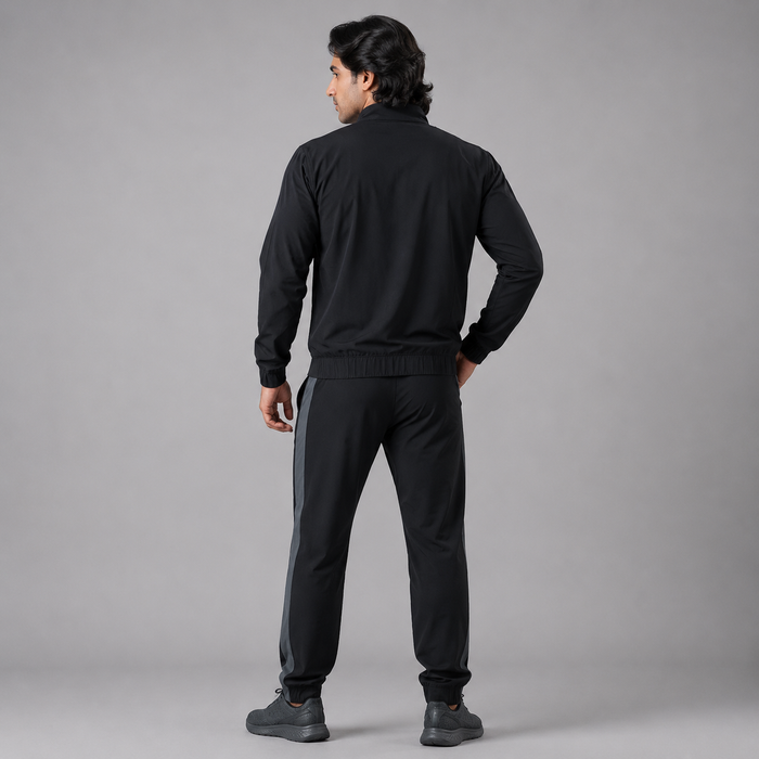 A man wearing a black tracksuit, viewed from behind, standing against a solid gray studio background.