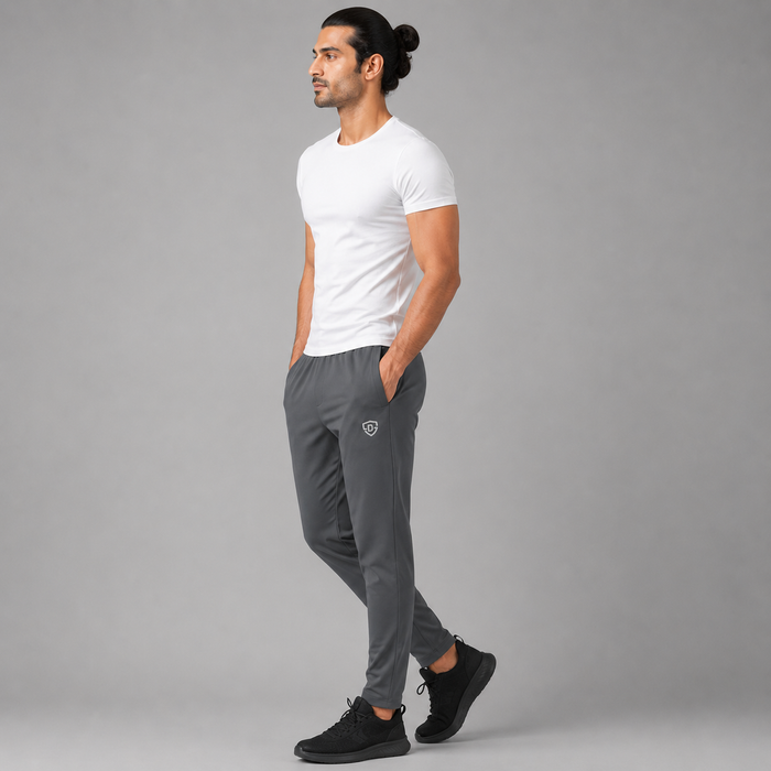 A man in a white t-shirt and gray jogger trousers / sweatpants walking in profile against a solid gray studio background.