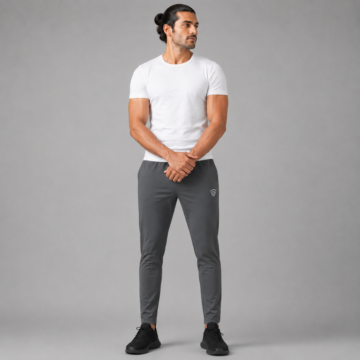 A man modeling a charcoal grey trousers, white crew-neck t-shirt and dark gray athletic jogger pants with black sneakers, standing against a solid gray studio background.