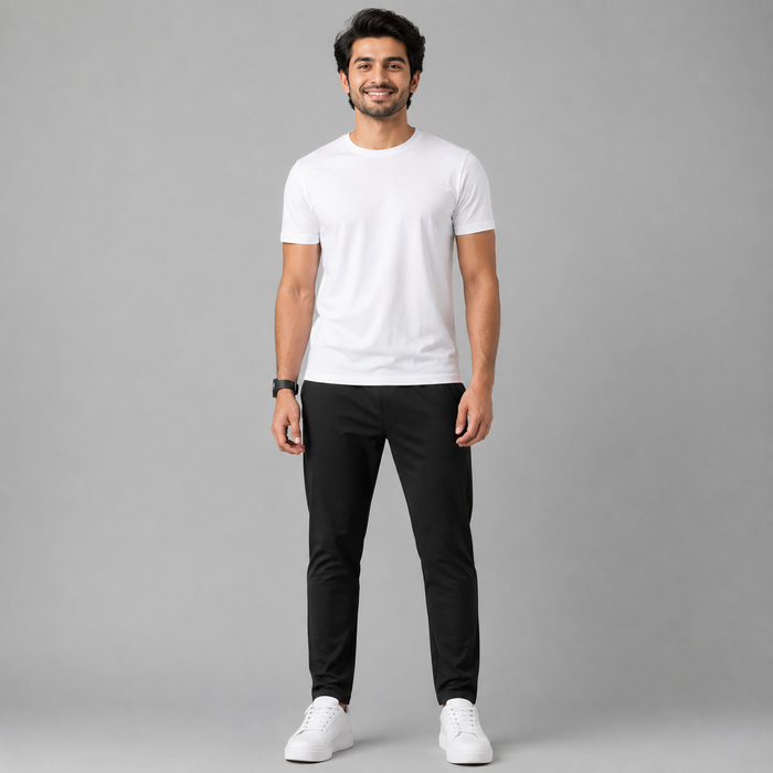 A man wearing a plain white short-sleeve crewneck t-shirt, black slim-fit pants, and white sneakers, standing against a solid gray studio background.