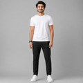 A man wearing a plain white short-sleeve crewneck t-shirt, black slim-fit pants, and white sneakers, standing against a solid gray studio background.