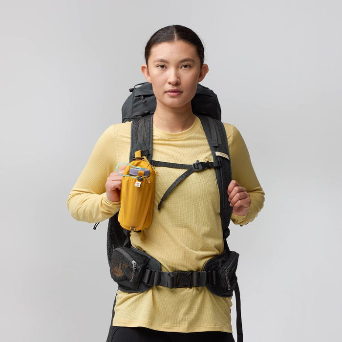 Person wearing a yellow shirt and black backpack with a gray background