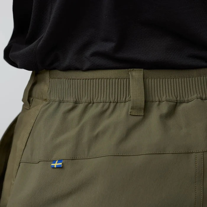 Close-up of olive green pants with a small flag patch on a plain background