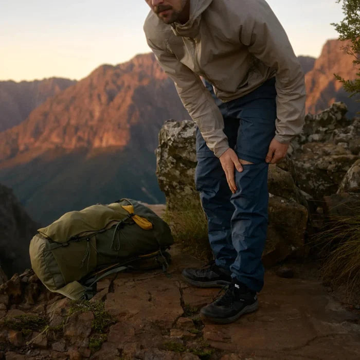 Man standing on a rocky outcrop with a backpack, surrounded by mountains.
