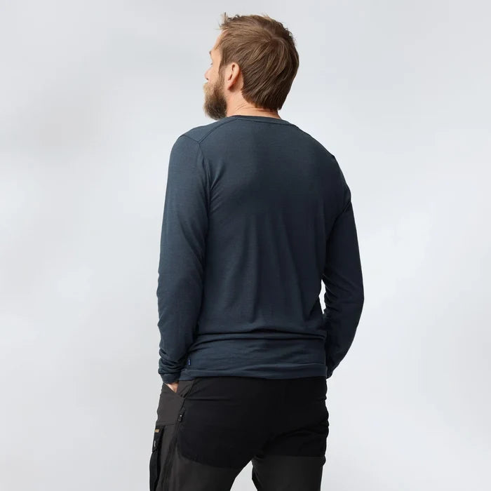 Man wearing a dark long-sleeve shirt and black pants on a light gray background