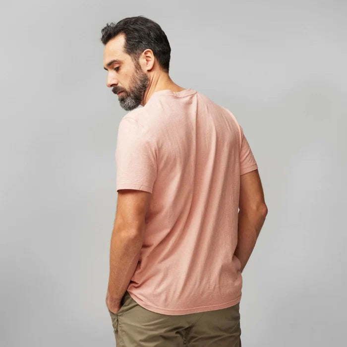 Man wearing a light pink t-shirt and green pants against a gray background