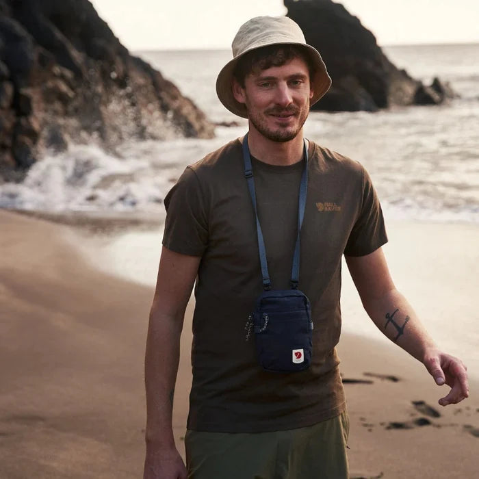 Man standing on a beach wearing a hat and carrying a blue bag