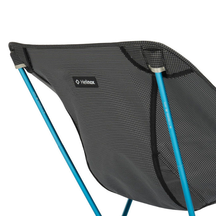 Black camping chair with blue legs on a white background, featuring the Helinox logo.
