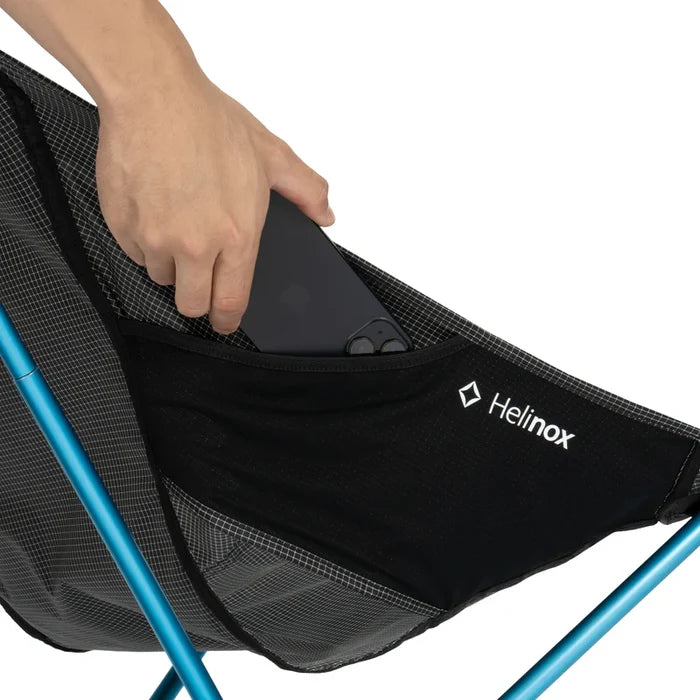Person placing a black item into a Helinox chair pocket on a white background