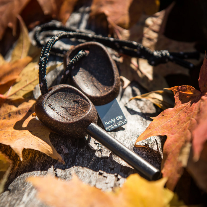 Two wooden fire starters with a black cord on a rock surrounded by autumn leaves.