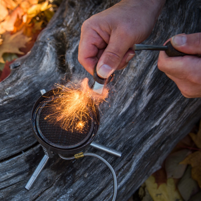 Person igniting a stove with a ferro rod on a wooden surface