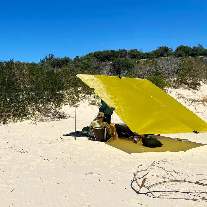 Yellow tarp set up in a sandy area with people underneath on a clear day.