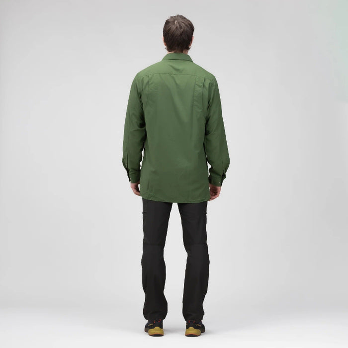 A man viewed from behind wearing an olive green long-sleeve shirt and black pants, standing against a light gray studio background.