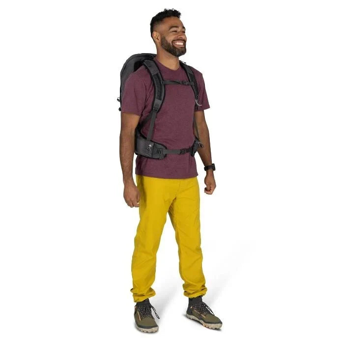 Man wearing a purple shirt, yellow pants, and a black backpack on a white background