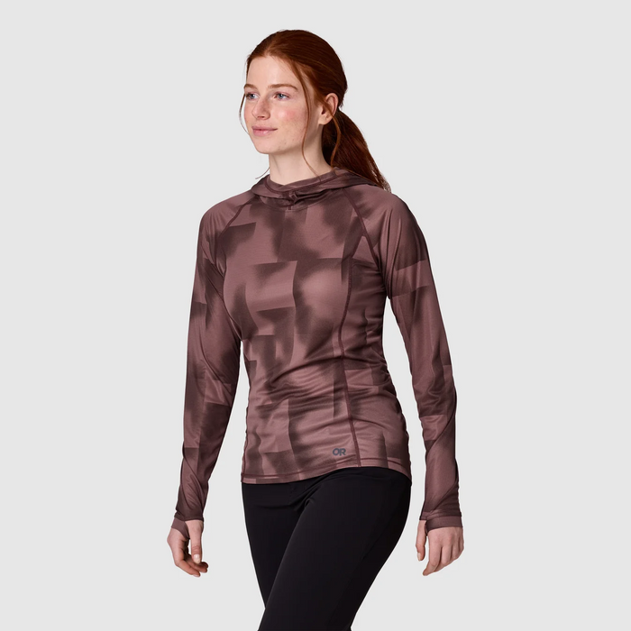 A woman wearing a long-sleeve athletic hooded top with a tonal geometric pattern in dusty mauve-brown, paired with black leggings, against a light gray studio background.