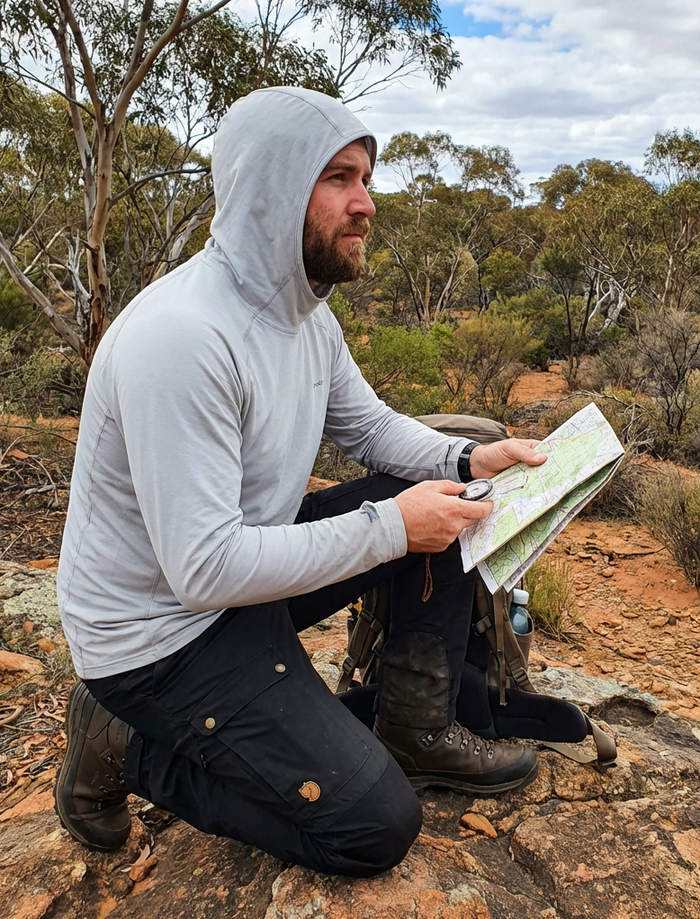 Man in outdoor setting, kneeling on rocky ground, looking at a map for land navigation course