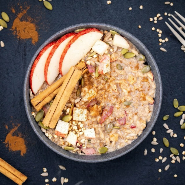 Bowling of oatmeal with apples, cinnamon, and seeds on a dark surface