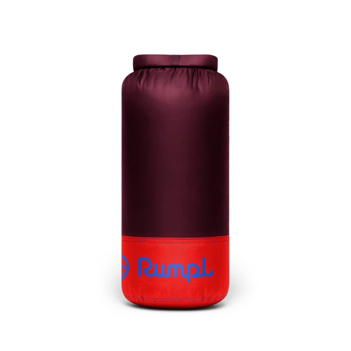 A cylindrical camping sleeping bag or insulated bag shown upright on a plain white background. The upper portion is a dark burgundy/plum color, and the lower portion is bright red with a blue 'Rumal' logo printed on it.
