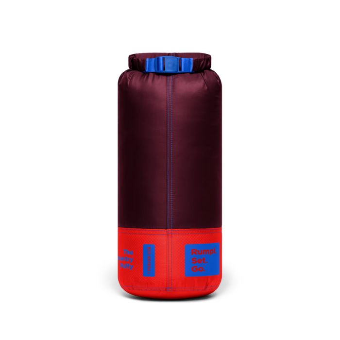 A cylindrical dry bag or storage sack in dark burgundy with a bright red base and blue accents, including a blue top closure and blue printed labels, shown on a plain white background.