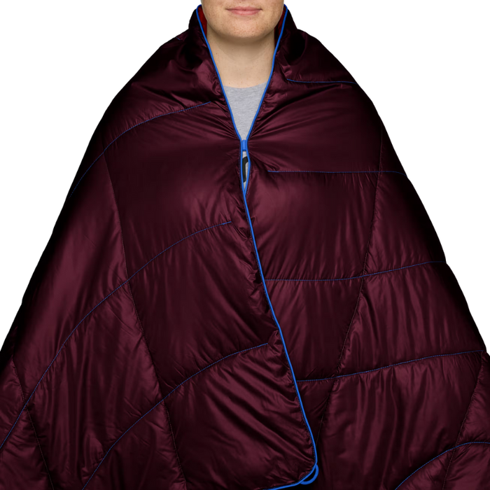 A person wrapped in a quilted puffer blanket or sleeping bag. The product is a deep burgundy/maroon color with bright blue piping and zipper trim, shown against a plain white background.