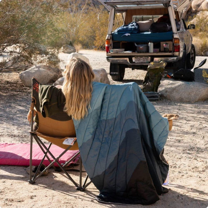 Person sitting outdoors with a vehicle and camping gear in the background