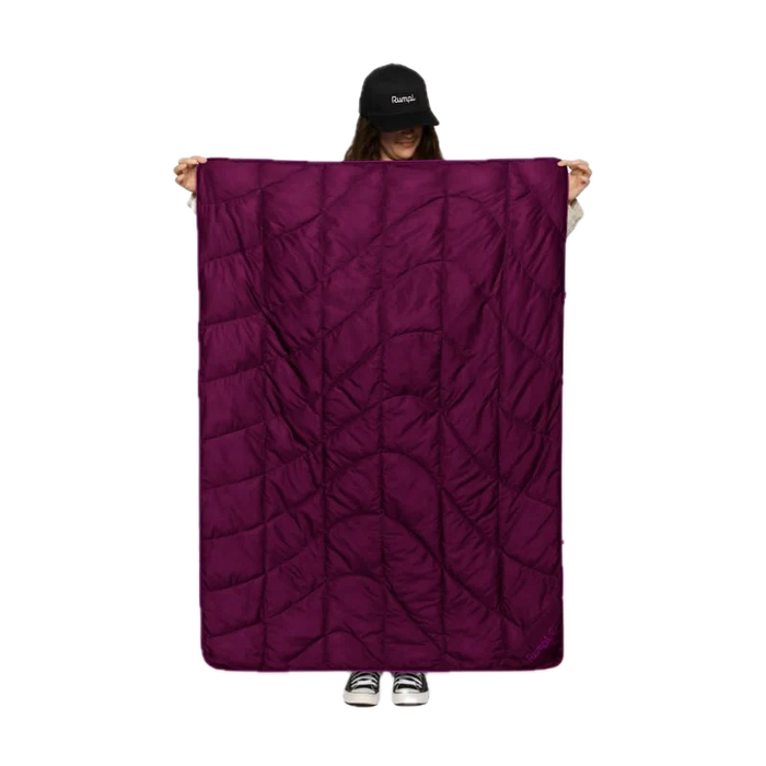 A person wearing a black cap holds up a large, dark purple quilted sleeping pad or camping blanket against a solid white background.