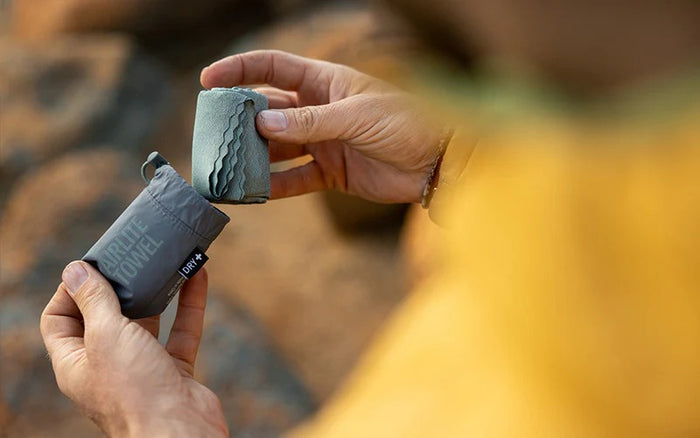Person holding two small cylindrical containers with labels against a blurred natural background