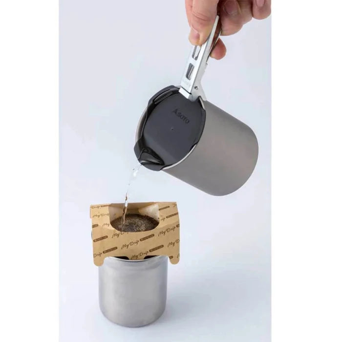 Person pouring liquid from a metal cup into a tea bag holder on a white background