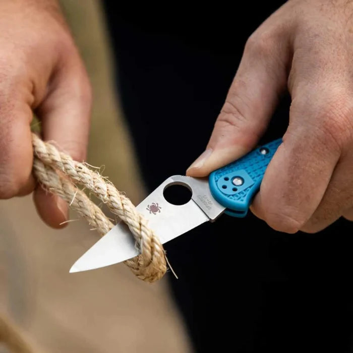 Person using a blue pocket knife to cut rope with a blurred background