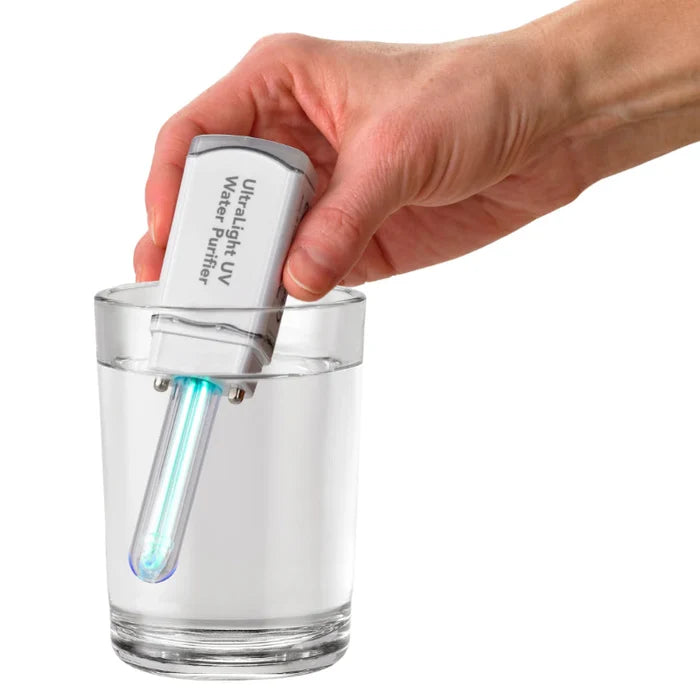 Hand holding a small UV water purifier over a glass of water on a white background
